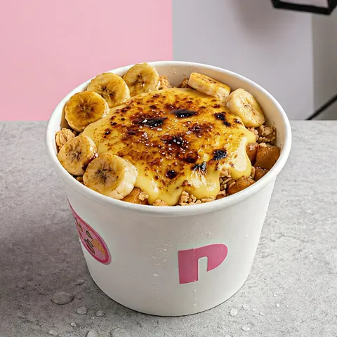 Banana crumble in a white peak cup: a torched custard top over granola, ringed with banana slices.