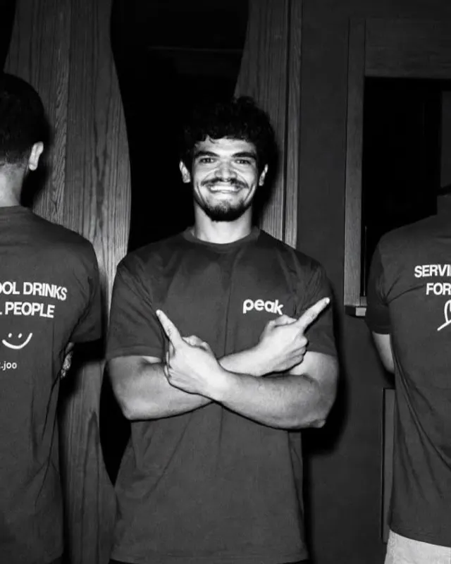 Hasan in a peak tee, arms crossed, pointing at his team's tees.