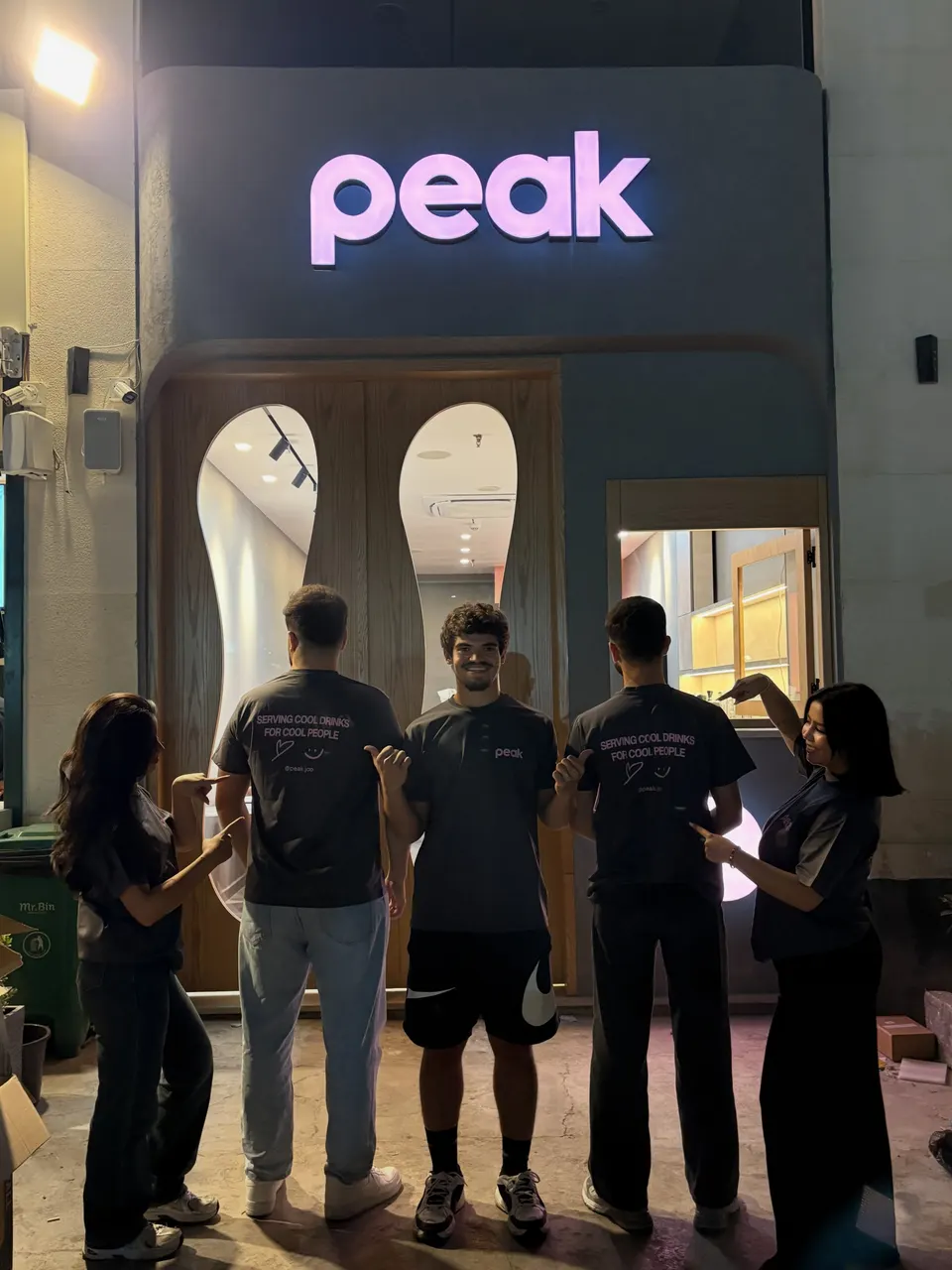 The peak storefront at night: the lit sign, wavy oak doors and the team out front.