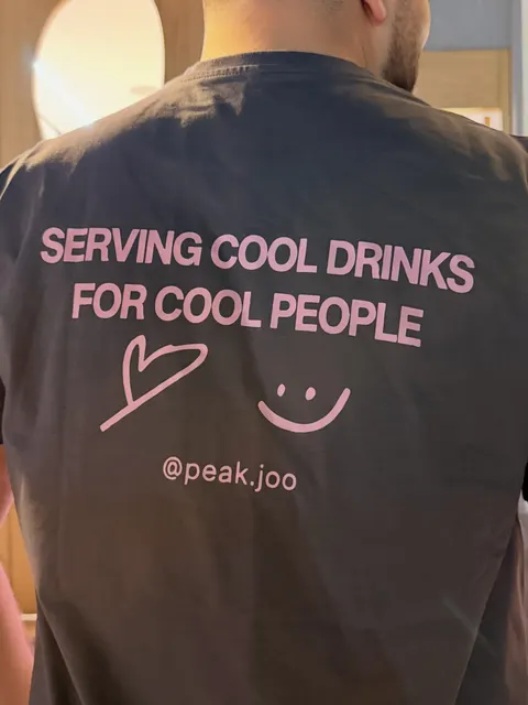 Back of a grey team tee printed in pink: Serving cool drinks for cool people, with a heart and a smiley.